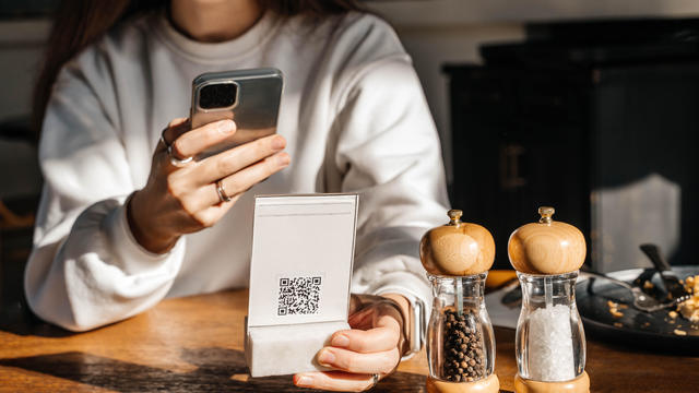 A beautiful young woman with long hair scans a QR code in a caf&eacute; to see the menu online. 